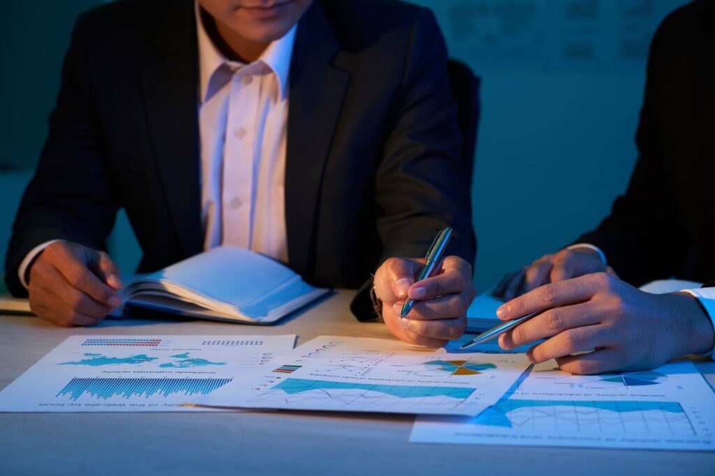 Deux professionnels en réunion analysent des graphiques et des données financières à l’aide de documents, dans un environnement de travail professionnel.