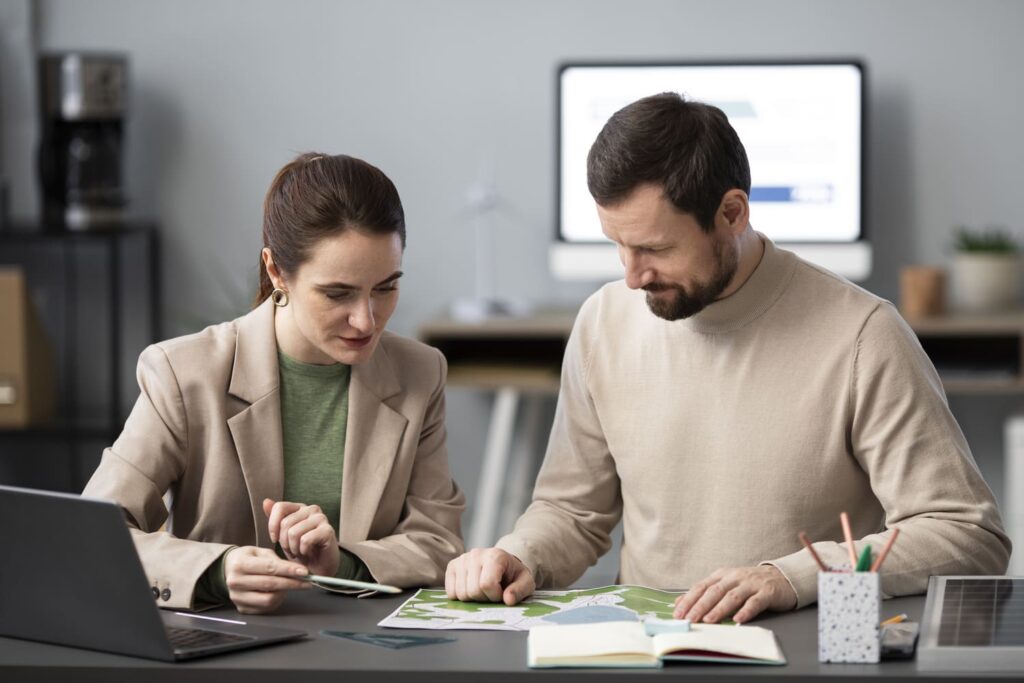 Deux professionnels collaborant autour d’un plan de travail, avec un ordinateur portable et des documents, illustrant le travail en équipe et le développement des compétences.
