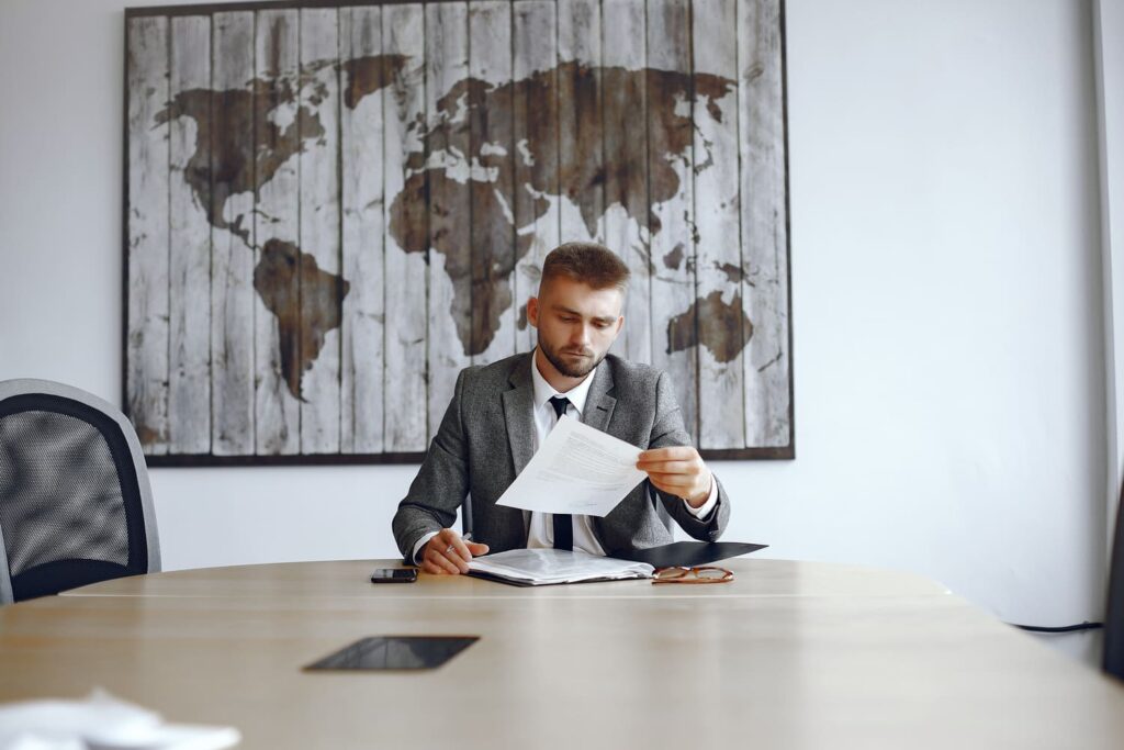 Homme d’affaires consultant un document dans un bureau devant une carte du monde, illustrant la gestion de patrimoine internationale.