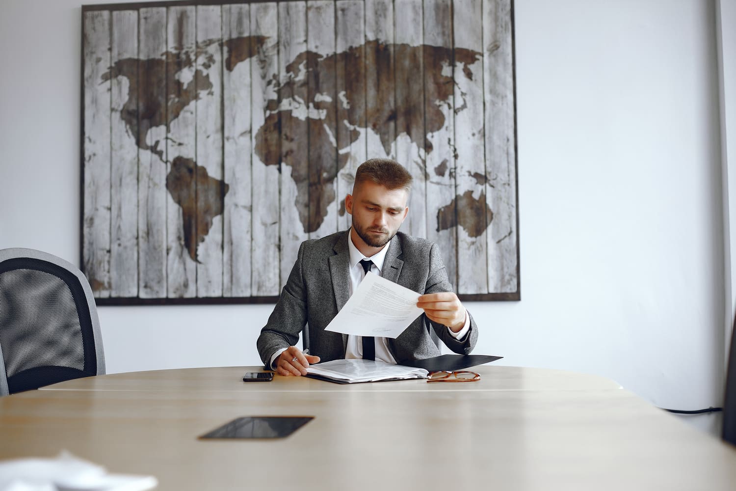 Homme d’affaires consultant un document dans un bureau devant une carte du monde, illustrant la gestion de patrimoine internationale.