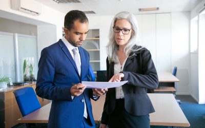 Successful businessman in suit reading document for signing and female grey-haired manager in eyeglasses pointing at something in report. Partners working in office. Business and management concept