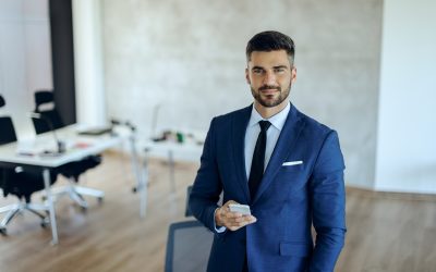 Homme en costume dans un environnement professionnel, tenant un smartphone et regardant l’objectif